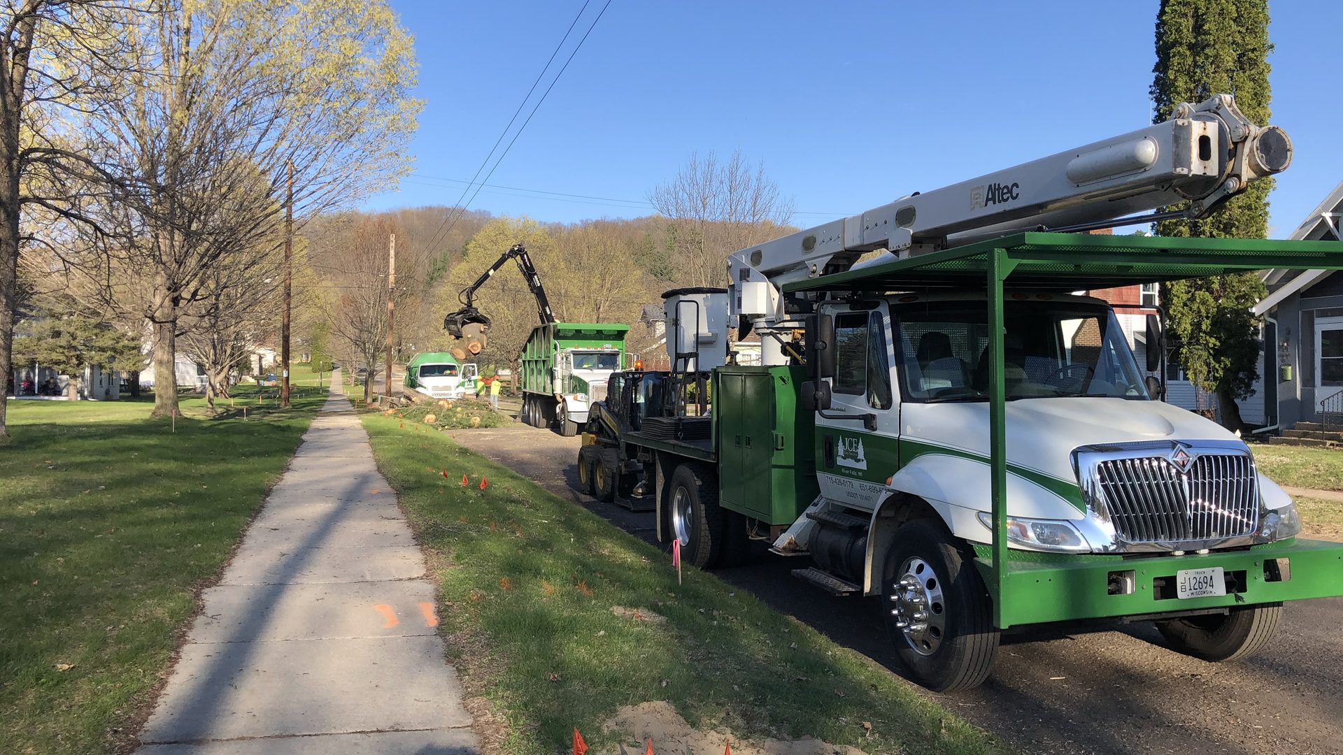 JCE Tree Service bucket trucks and chip trucks lined up on a residential street