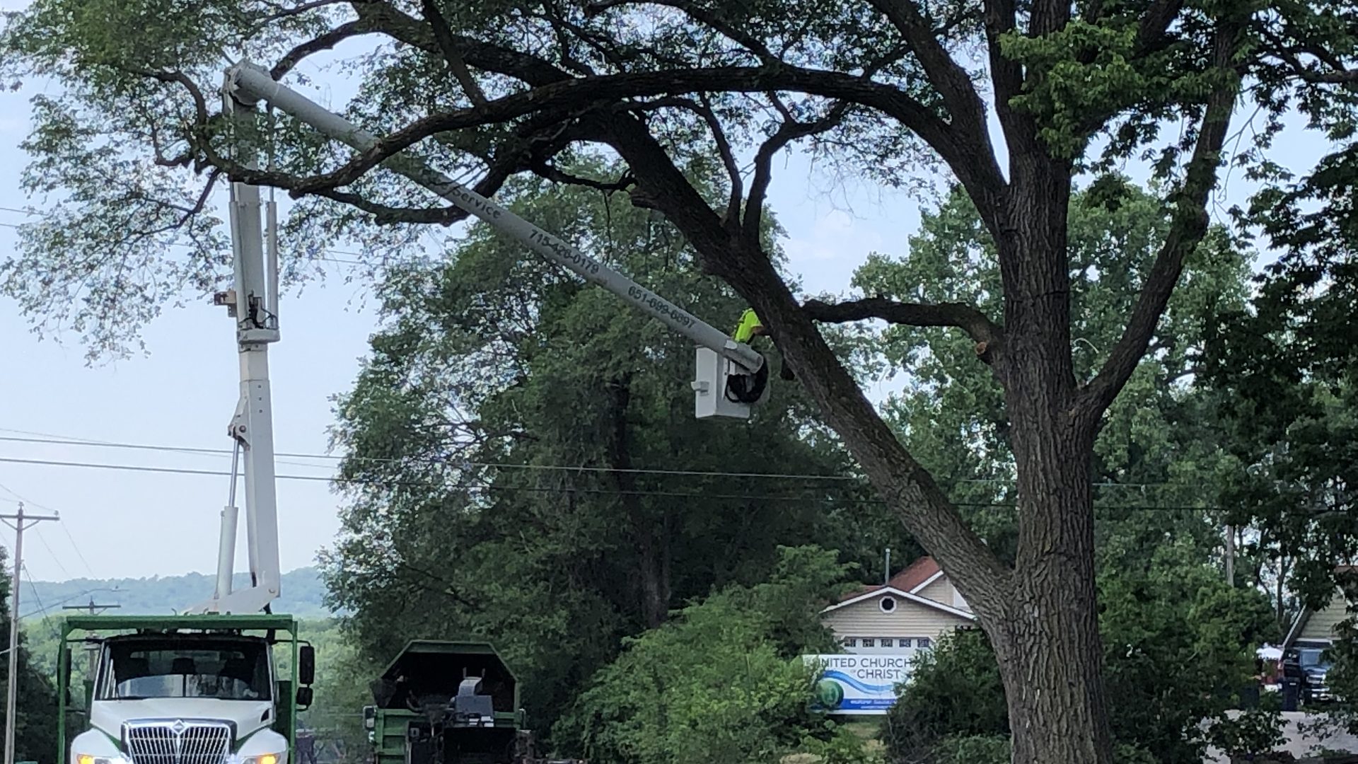 A JCE bucket truck parked beneath a mature tree on a quiet residential street