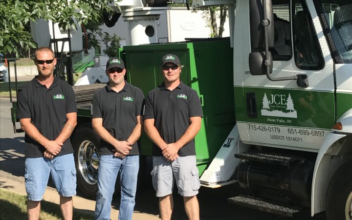 Three men stand in front of a bucket truck.