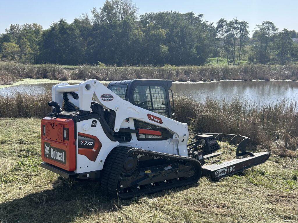 Bobcat track loader mowing brush near a pond in Prescott, WI
